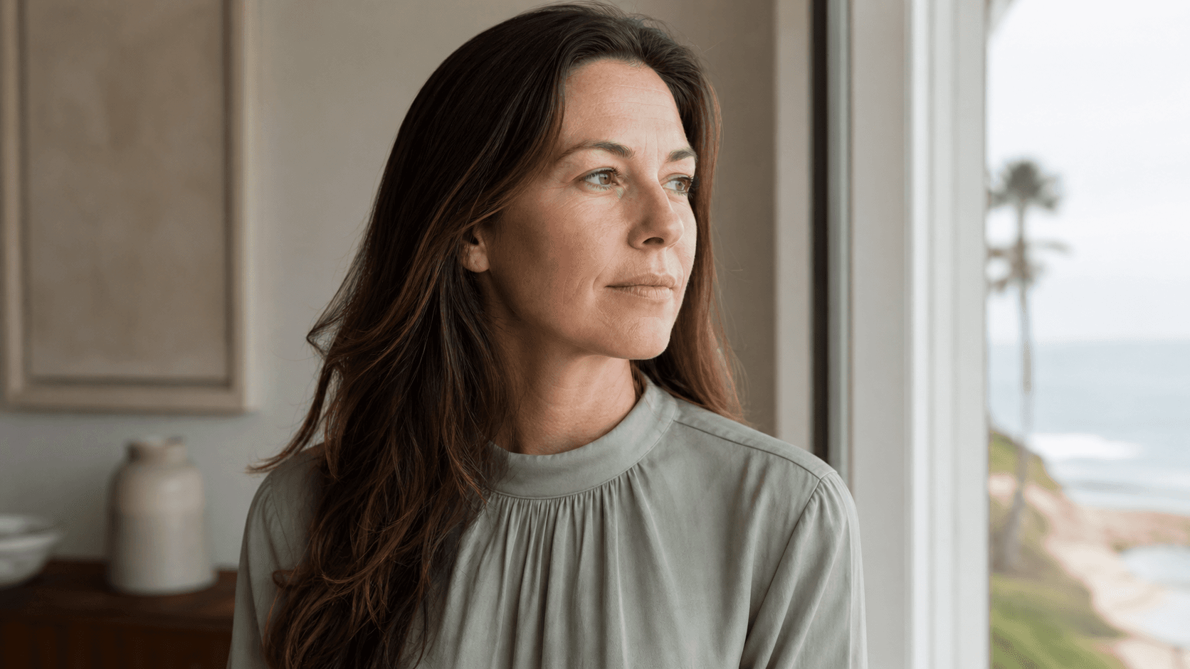 Woman viewing her natural skin texture in soft window light before a consultation