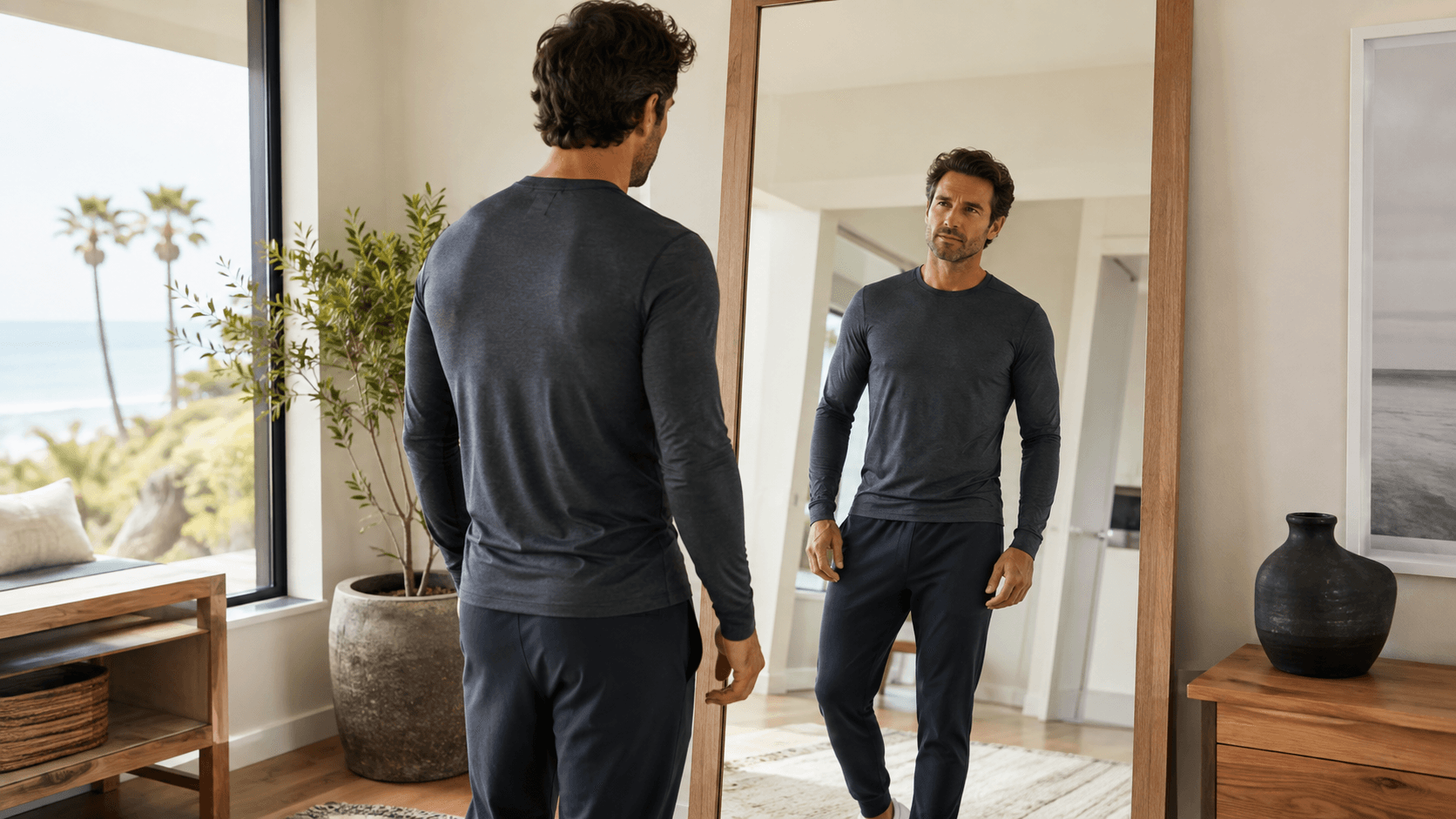 Fully clothed athletic man evaluating his torso proportions in a bright coastal room